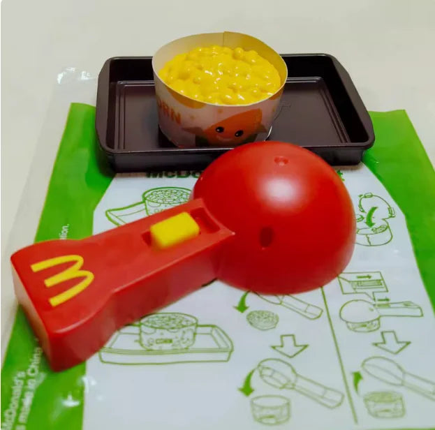 ألعاب بيت اللعب من ماكدونالدز، تشمل مجسمات مكونات المطعم، صناديق وجبات، ماكينات الطلب، وقبعات للأطفال، نموذج لعب واقعي